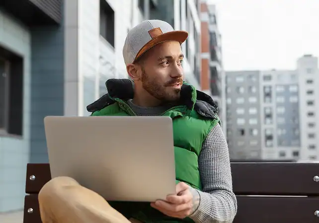 Urban man with laptop sitting on a bench in city.