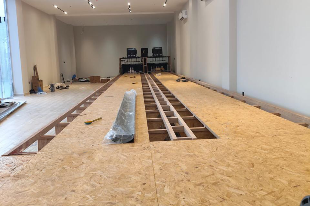 Bowling lane construction with wooden flooring and pin-setting equipment in progress.